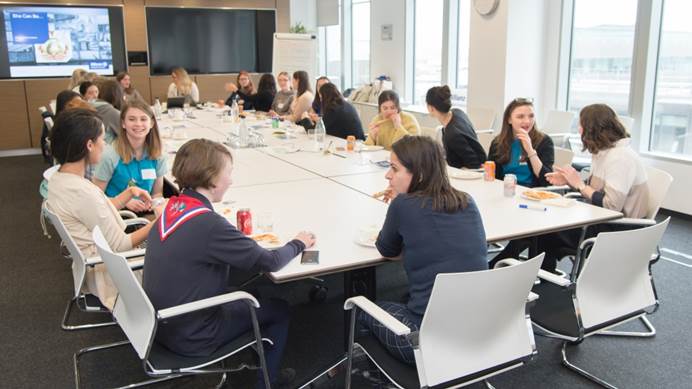 Group of young women talk to each other around a board room table
