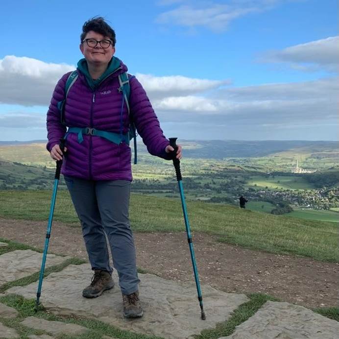 Kate, a smiling white woman with short hair, stands on a Peak District hill
