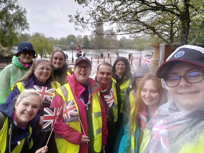 10 volunteers stand in front of the River Thames. It's raining, but they're all smiling and waving Union Flags